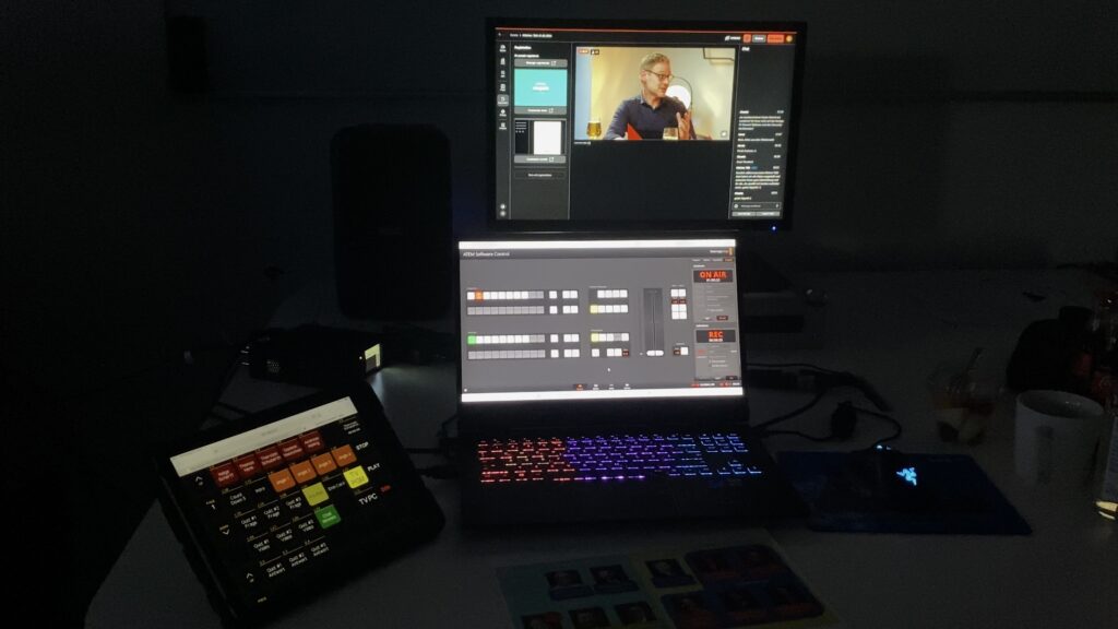 Zwei Bildschirme zur Steuerung des Tons bei einer Livestreamproduktion, im Hintergrund sieht man den aktuellen Livestream